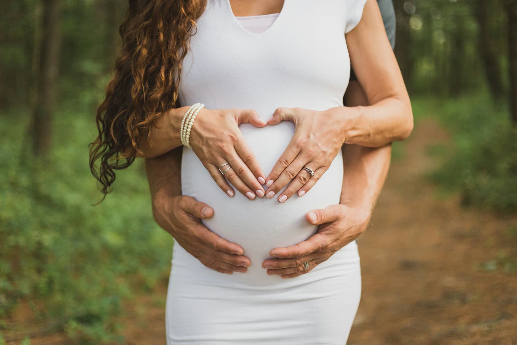 Expectant parents holding their hands in a heart shape over a pregnant belly