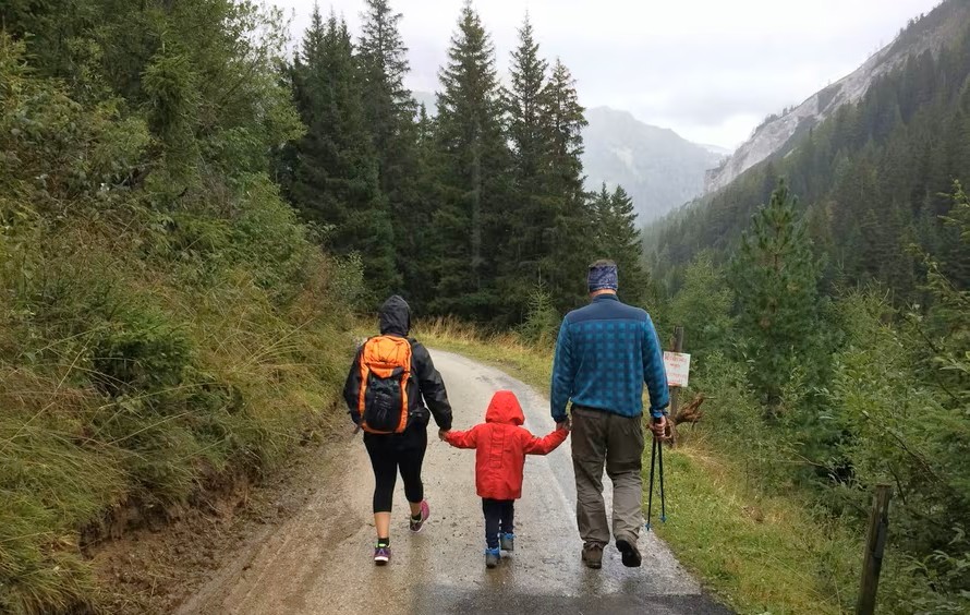 A family walking hand in hand up a mountain path in the rain, seen from behind.